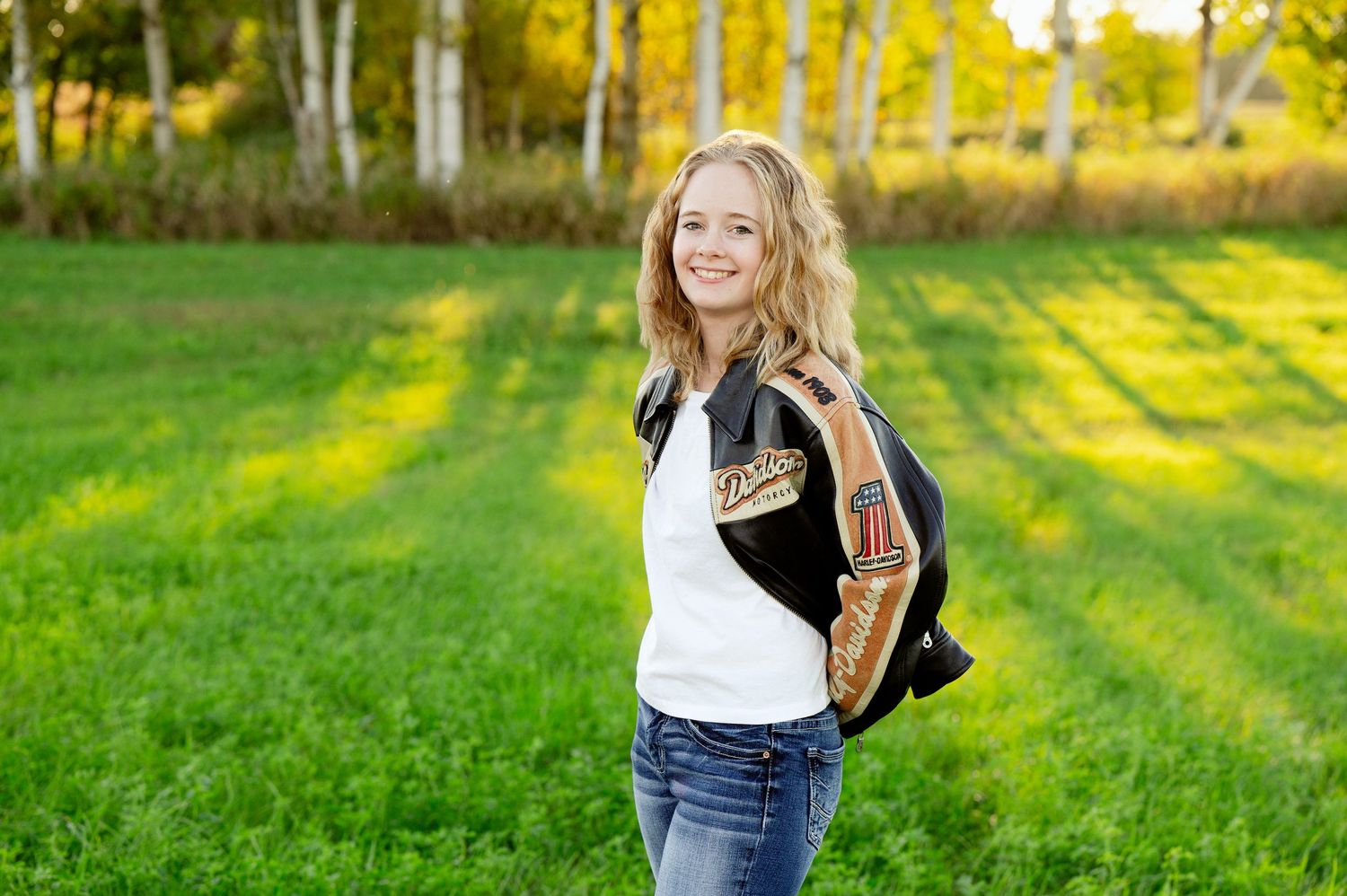 Senior Portrait in Foreston MN Student stands in sunny field with autumn birch trees in background.