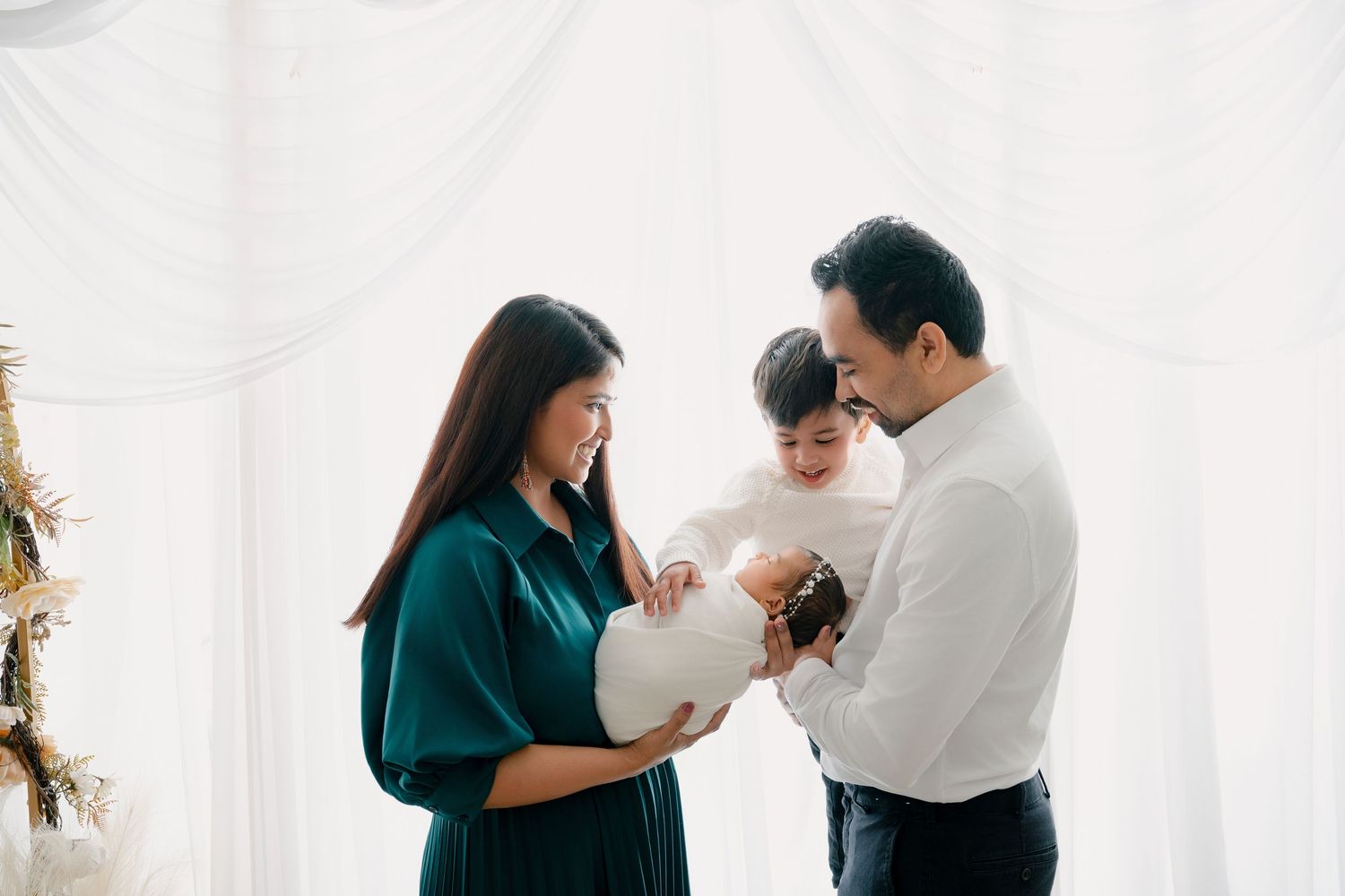 Studio family photo with white draped backdrop and emerald green dress.