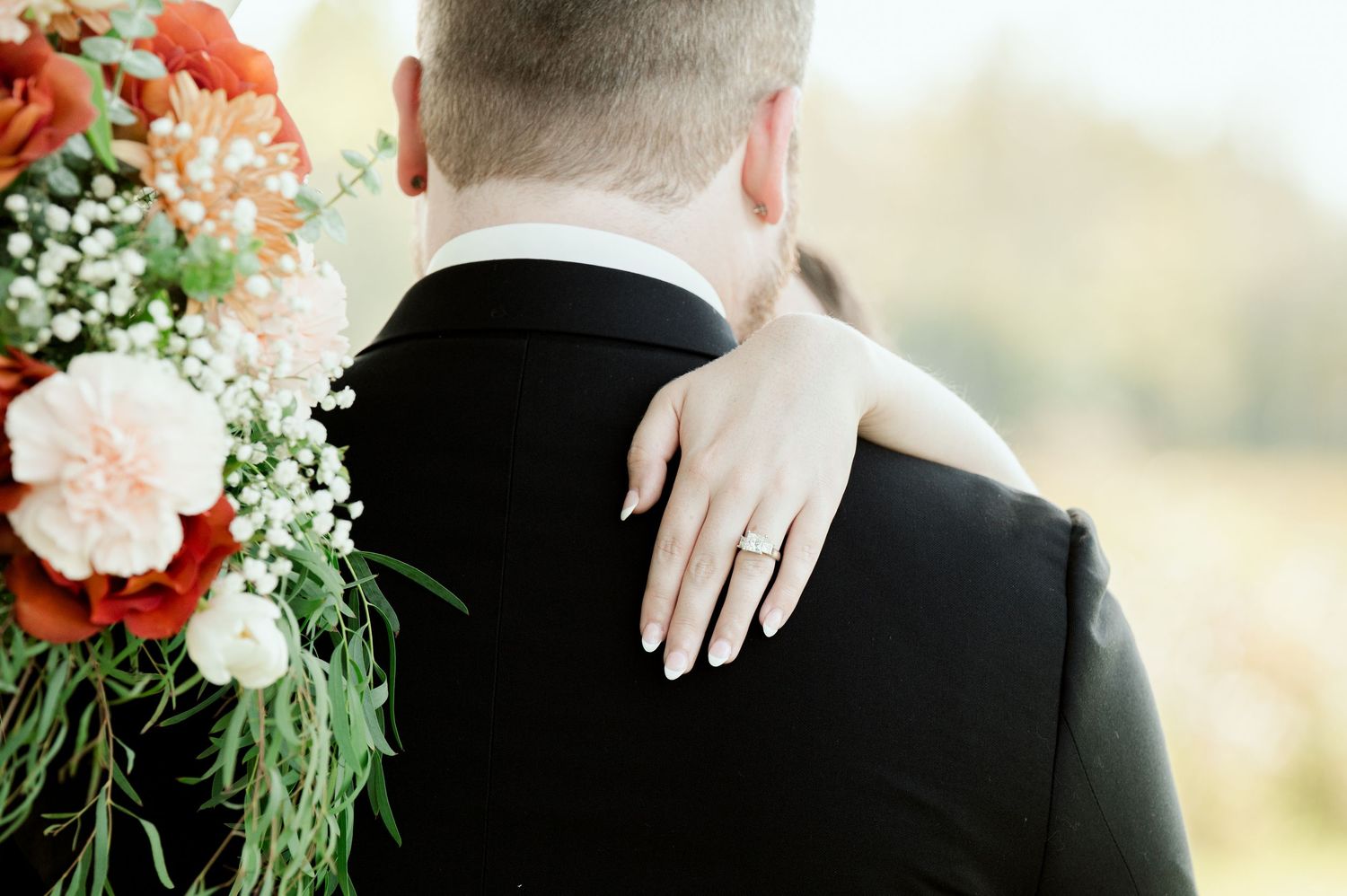The Grands at Mulligans- Wedding Photos: portrait showing couple embracing with coral and white floral bouquet details.