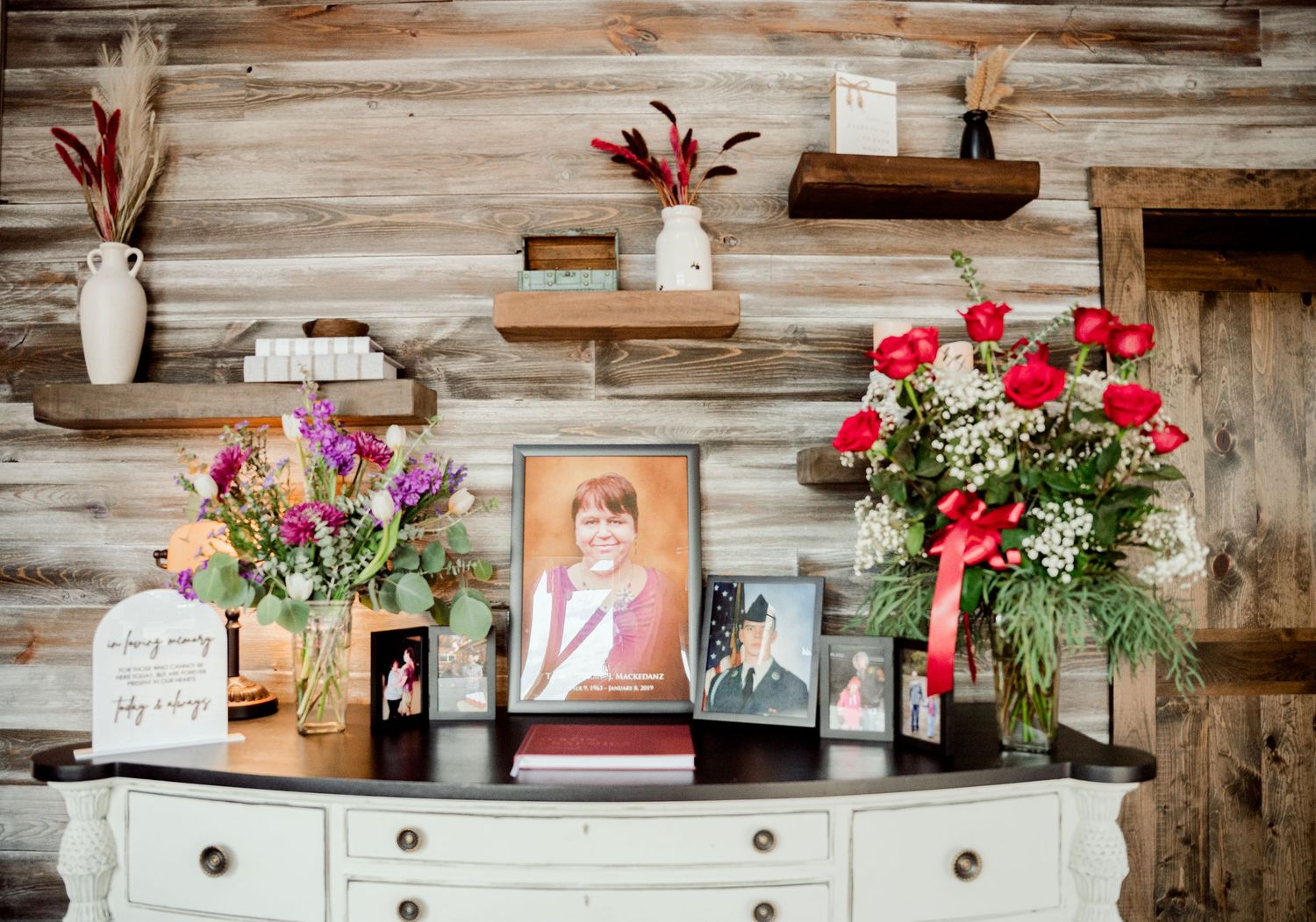 The Grands at Mulligans- Wedding Photos: A rustic display shelf with framed photos and floral arrangements on a wooden wall.