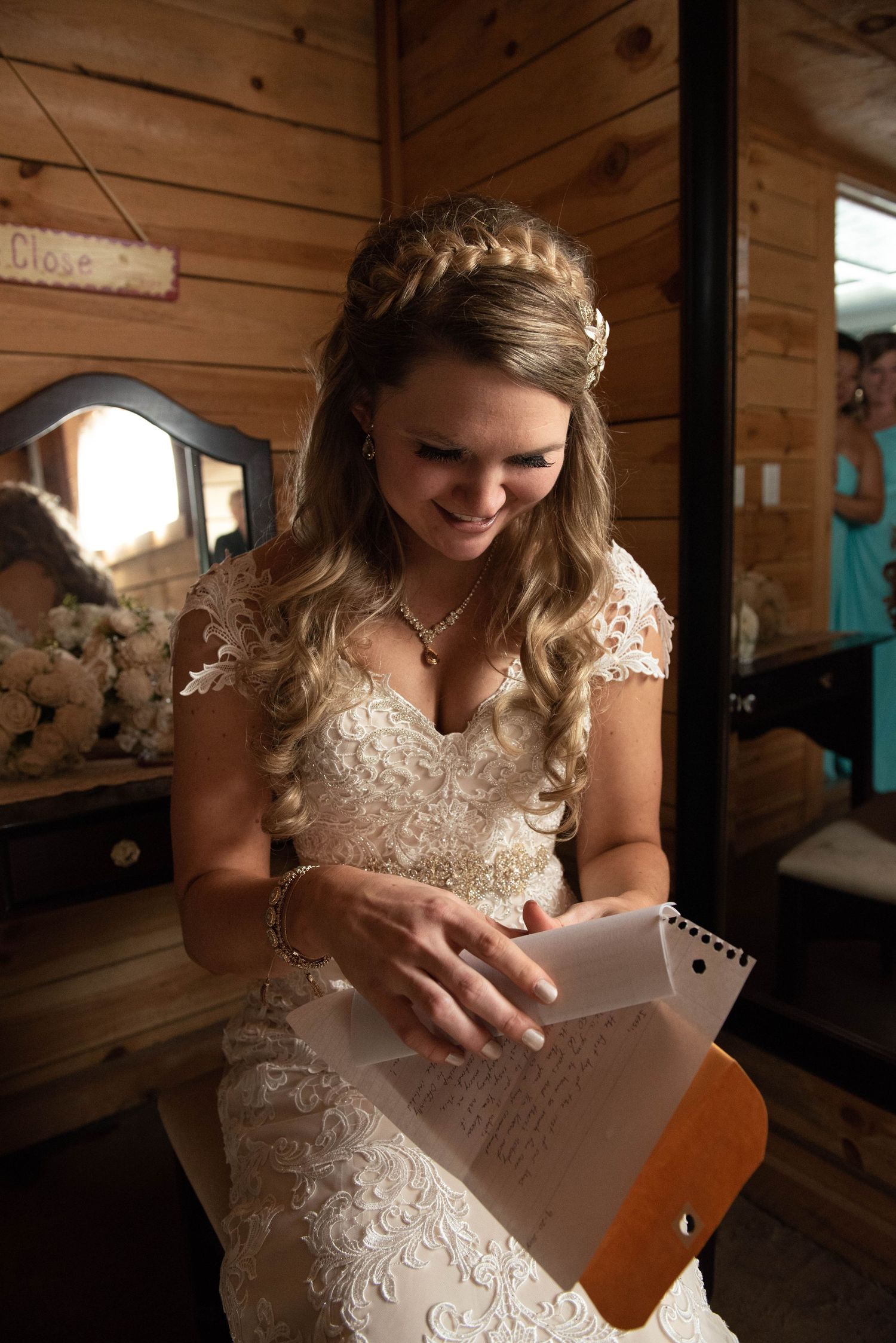 A person in a wedding dress reads a letter in a rustic wooden cabin setting.
