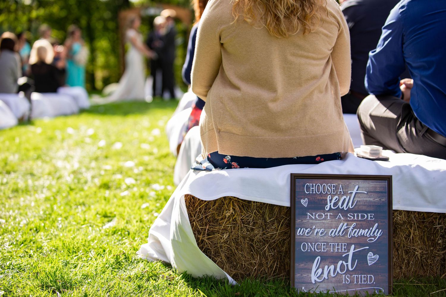 A rustic wedding sign sits on a white tablecloth during an outdoor ceremony. Rum River Barn Milaca Minnesota Weddings
