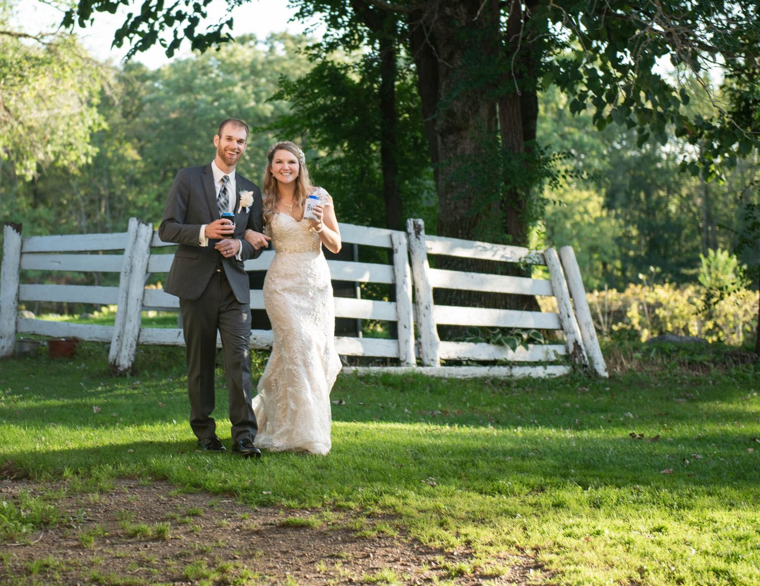 Couple walking together on grass path alongside white fence on wedding day. Rum River Barn Milaca Minnesota Weddings