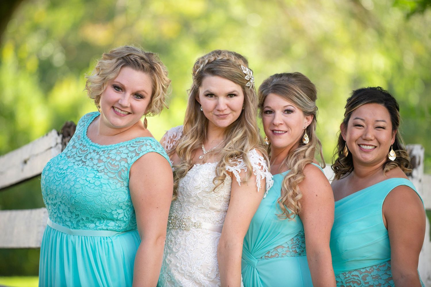 A wedding party smiles together in coordinated turquoise dresses against a rustic backdrop. Rum River Barn Milaca Minnesota Weddings