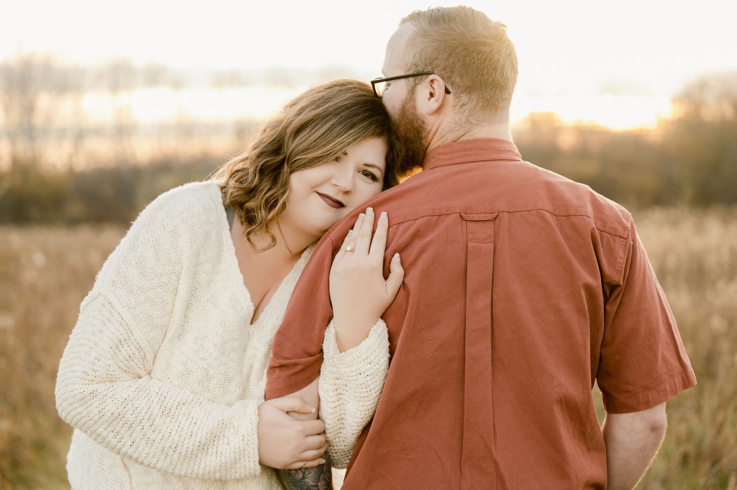 A couple shares an intimate embrace in a wheat field during golden hour sunset.