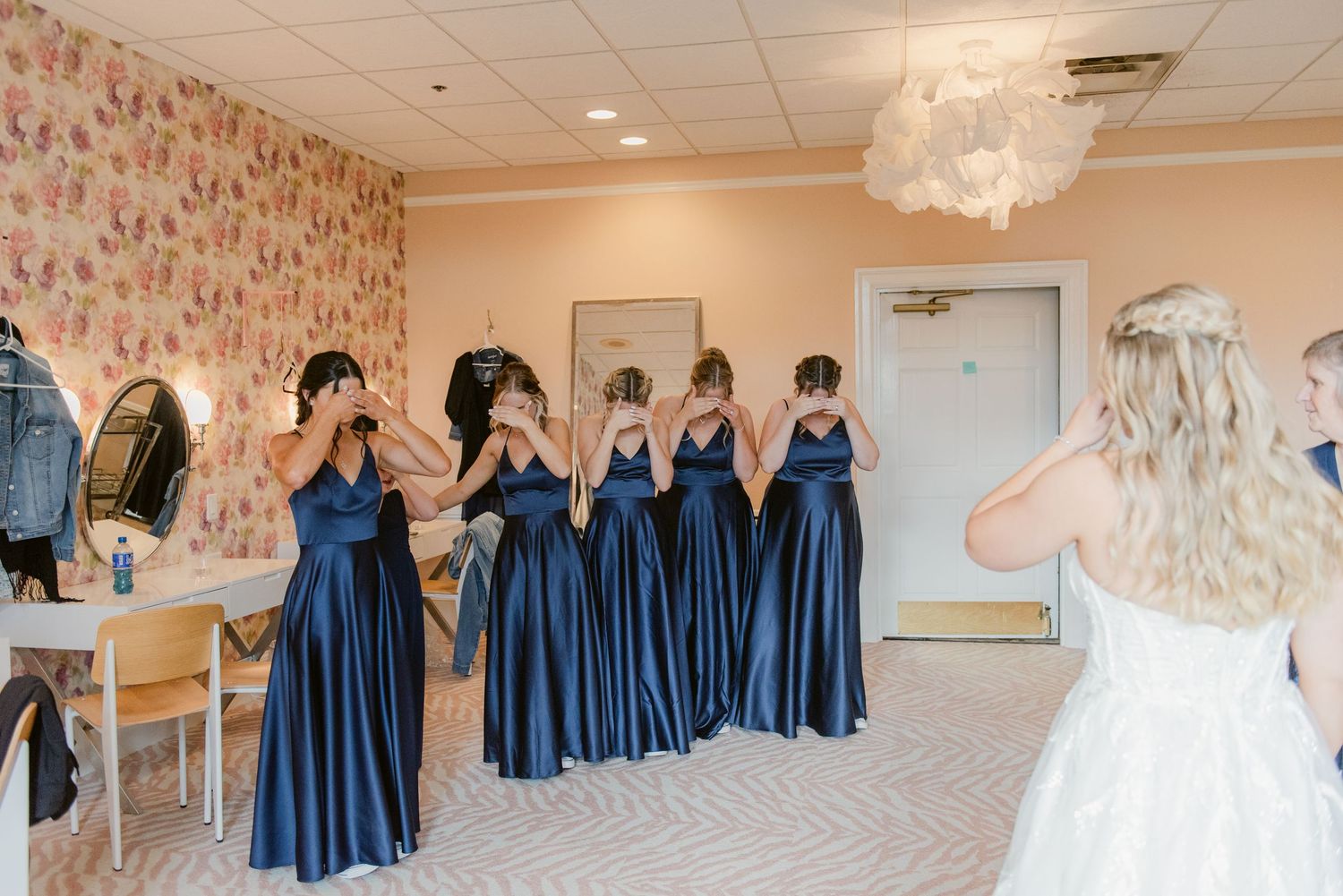 Bridesmaids in navy blue dresses cover their eyes for a first look reveal moment.