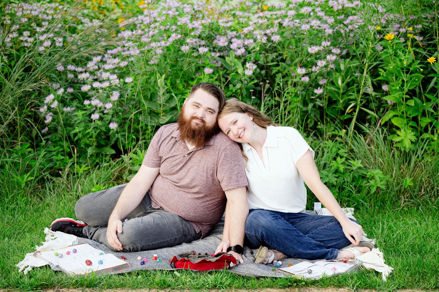 St cloud area engagement photos. A couple relaxes together on a picnic blanket in a meadow with blooming wildflowers on a sunny day.