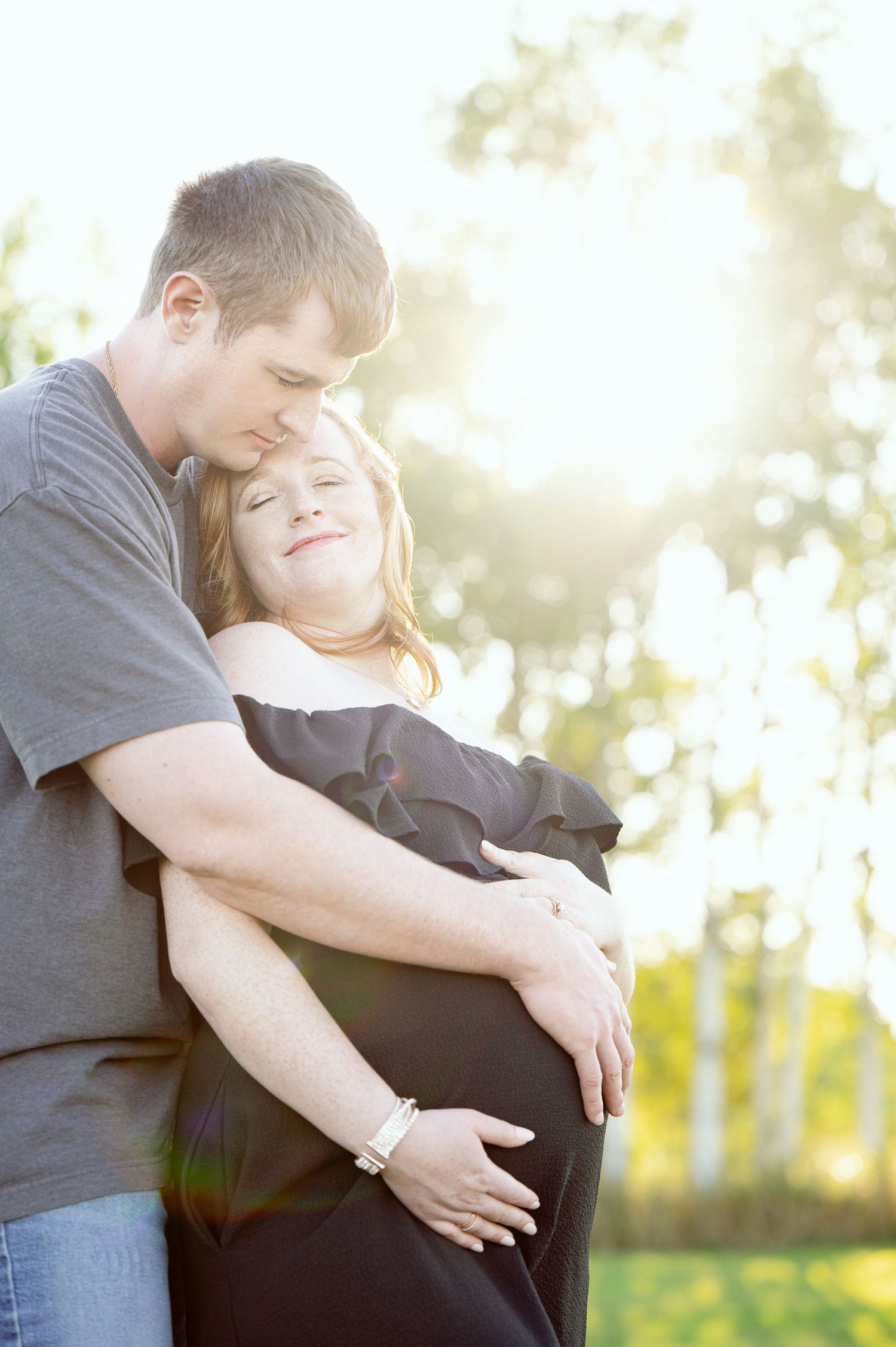 A tender maternity moment captured in golden sunlight among aspen trees.