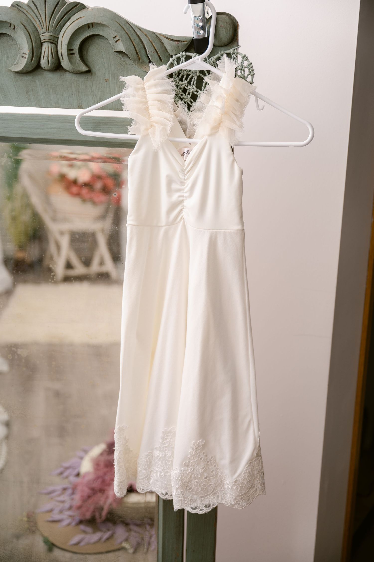 A delicate white sleeveless dress with lace trim detail hangs on a white plastic hanger against a vintage-style background.