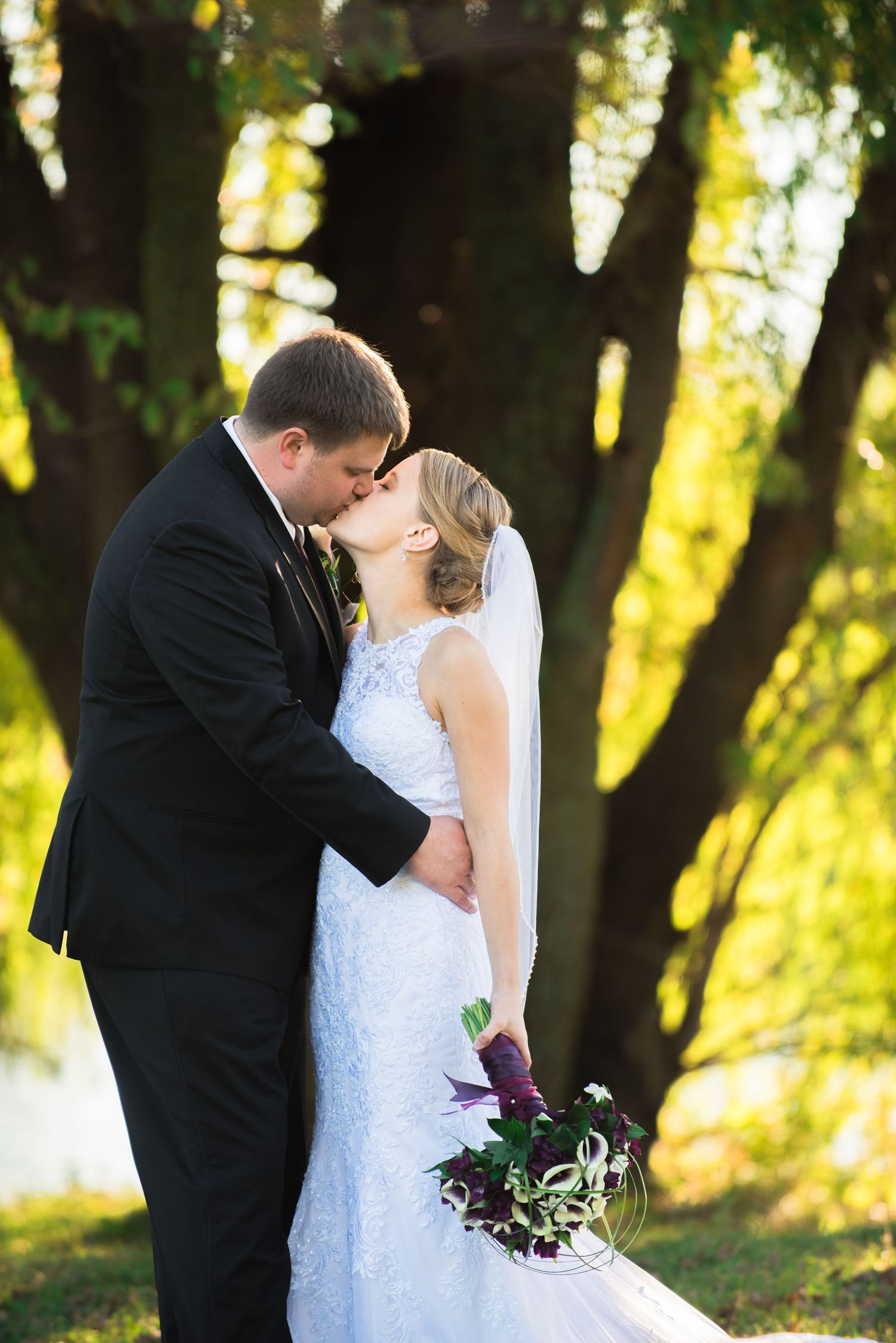 Newlywed couple sharing romantic kisses in a scenic outdoor setting with golden sunlight filtering through trees. Andover wedding at Magesti