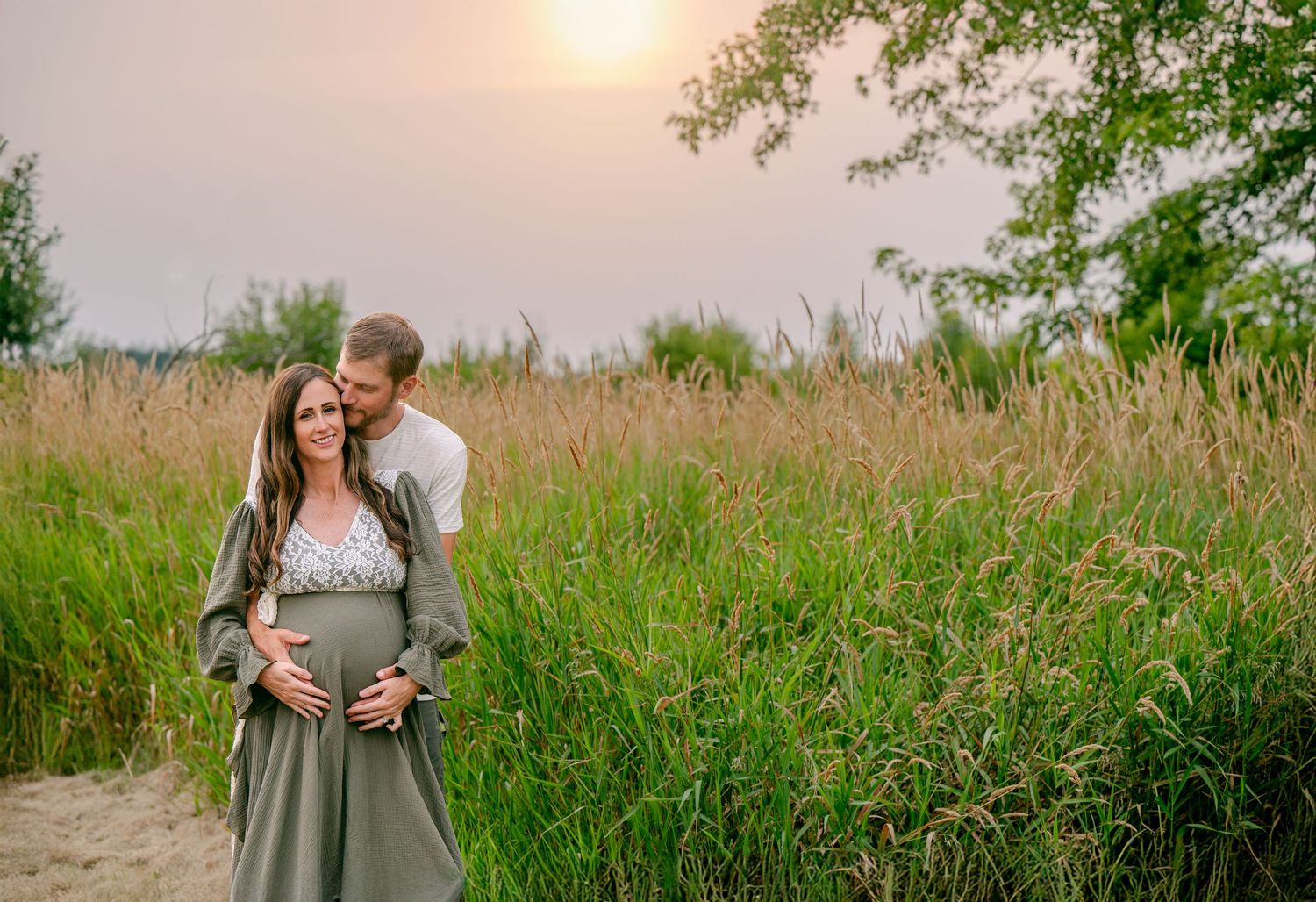 Intimate maternity photo of couple embracing in a golden sunset field with tall grasses.