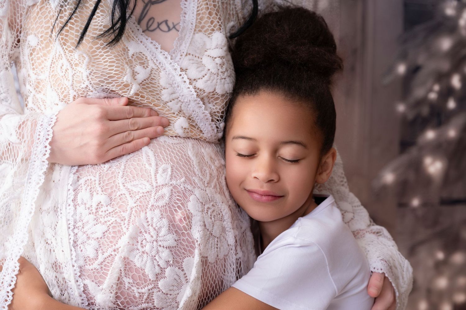 Child hugging pregnant mother's belly with eyes closed in dreamy pose.