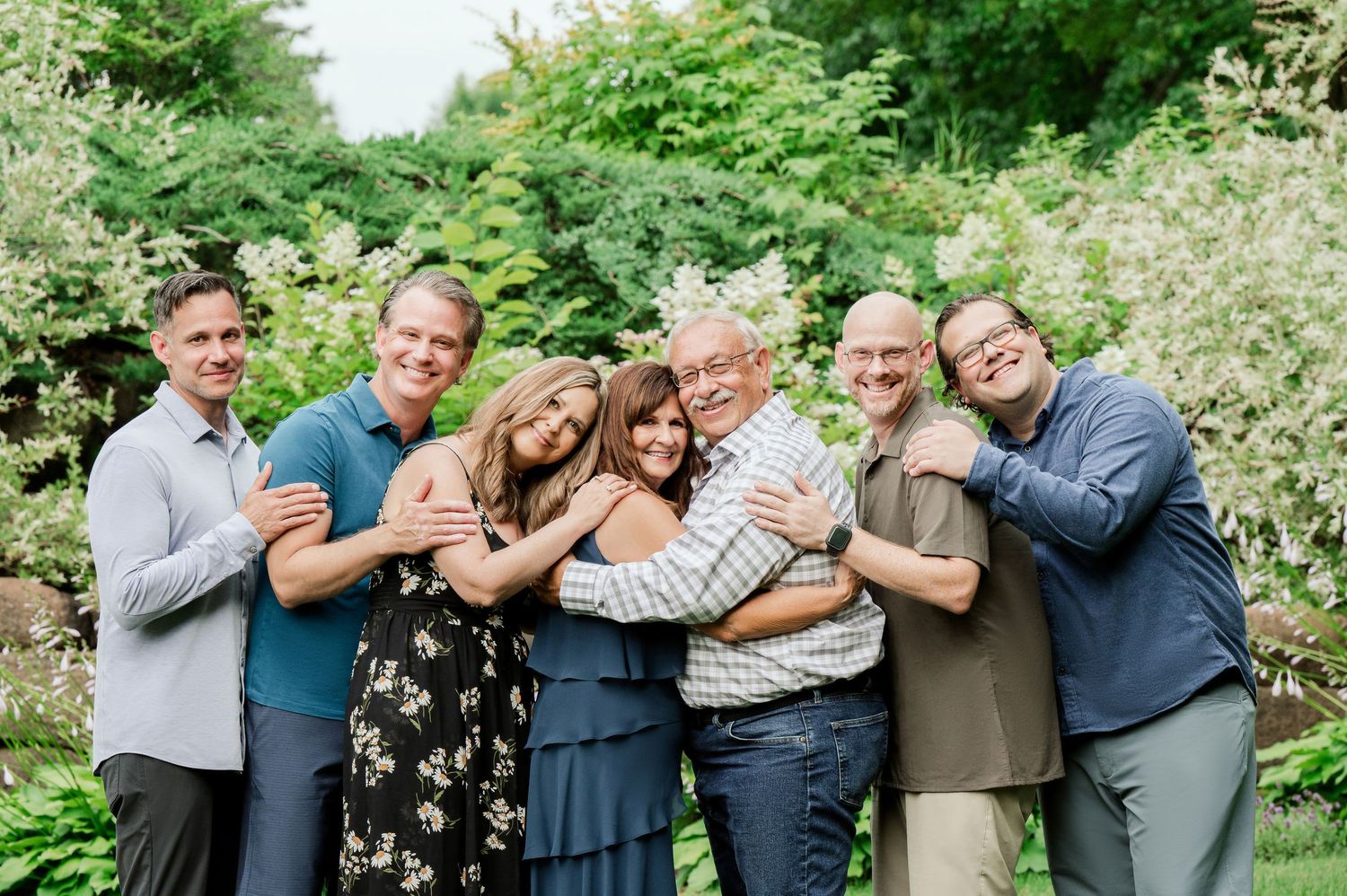 Clear Lake Family Photography: A group photo of family members hugging together outdoors with green foliage in the background.