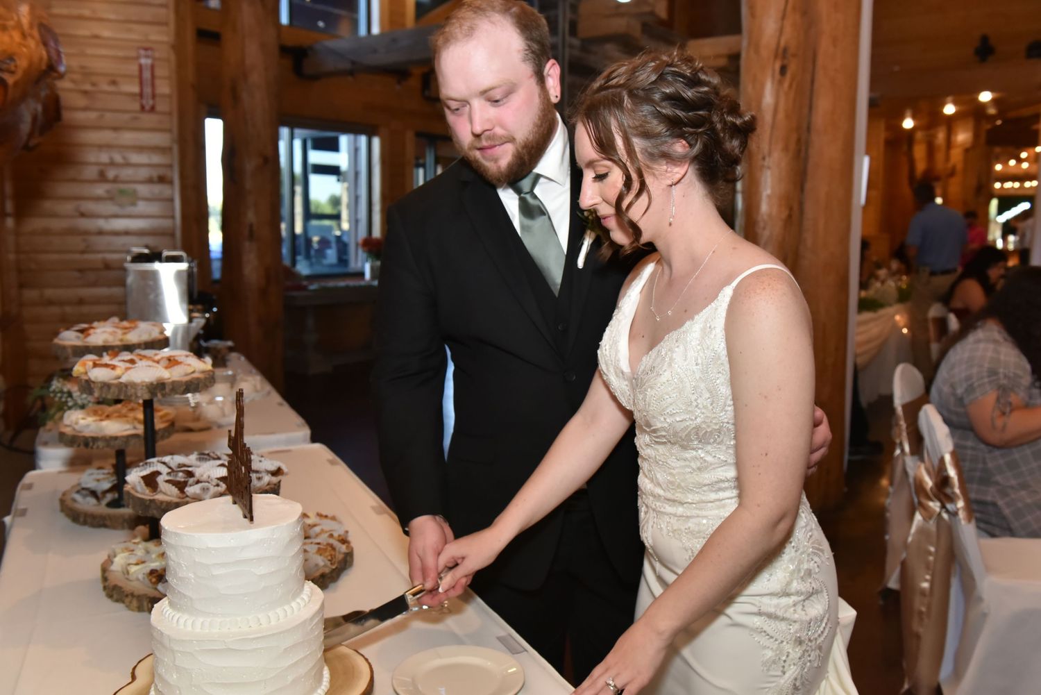 The Grands At Mulligans. A couple shares an intimate moment while cutting their tiered wedding cake at a rustic indoor reception.