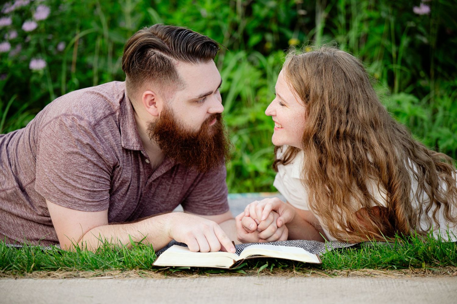 Two people lying on grass sharing a book moment together in a garden setting.