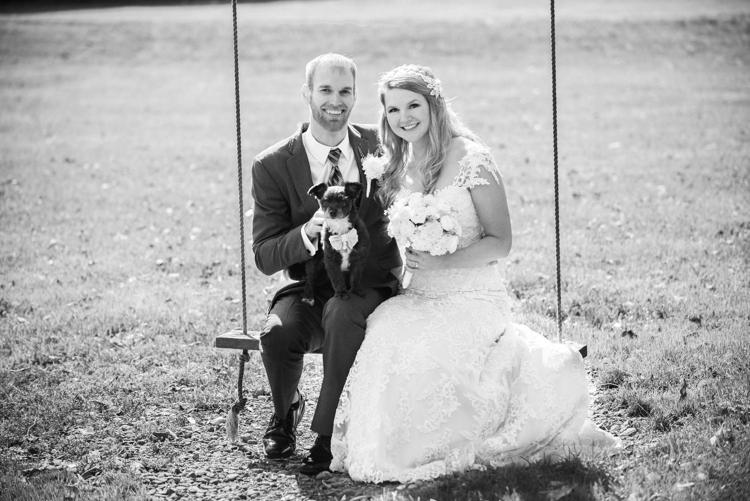 Wedding couple sitting on swing holding small dog in black and white photo. Rum River Barn Milaca Minnesota Weddings
