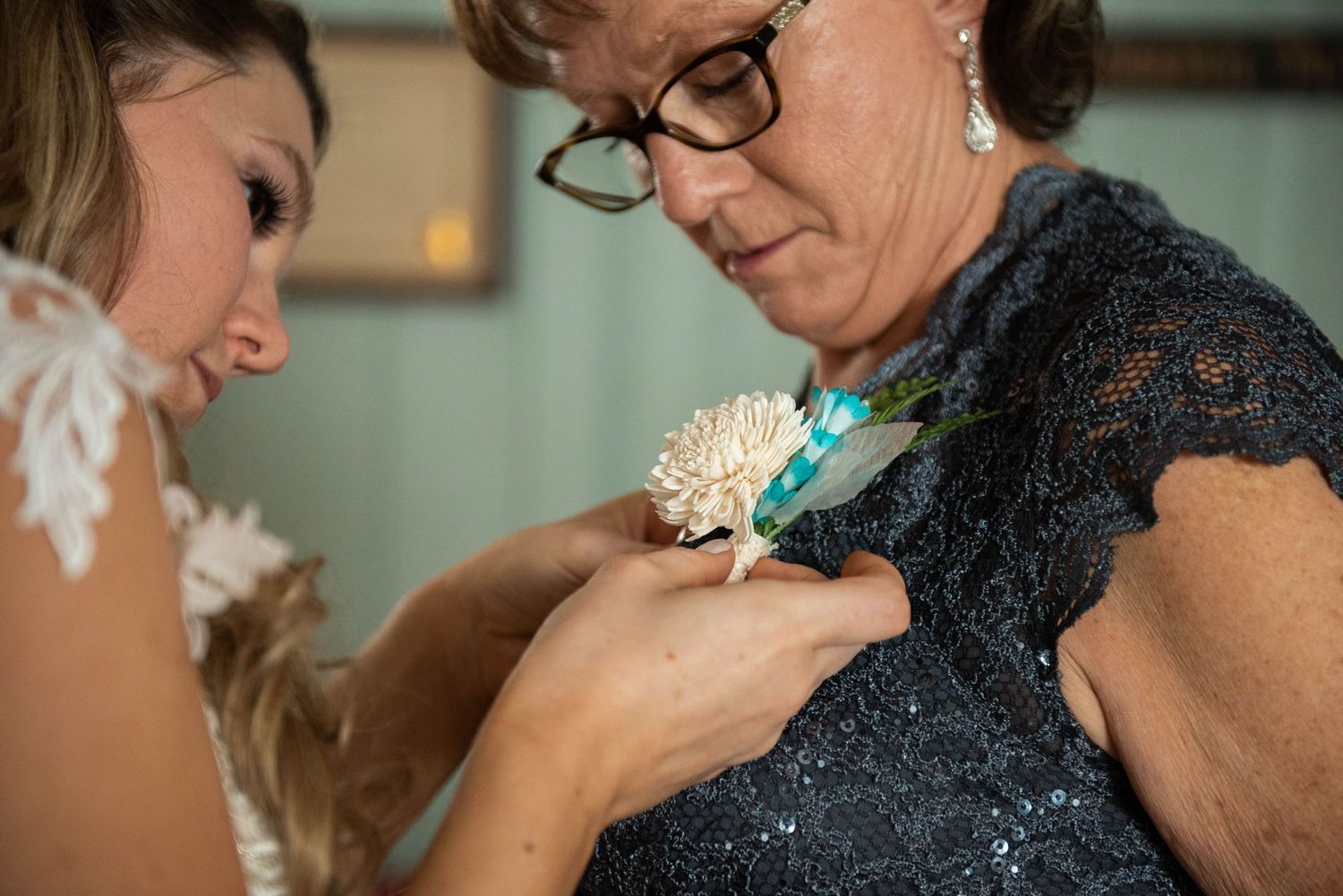 A delicate cream corsage being pinned onto a navy blue lace dress.