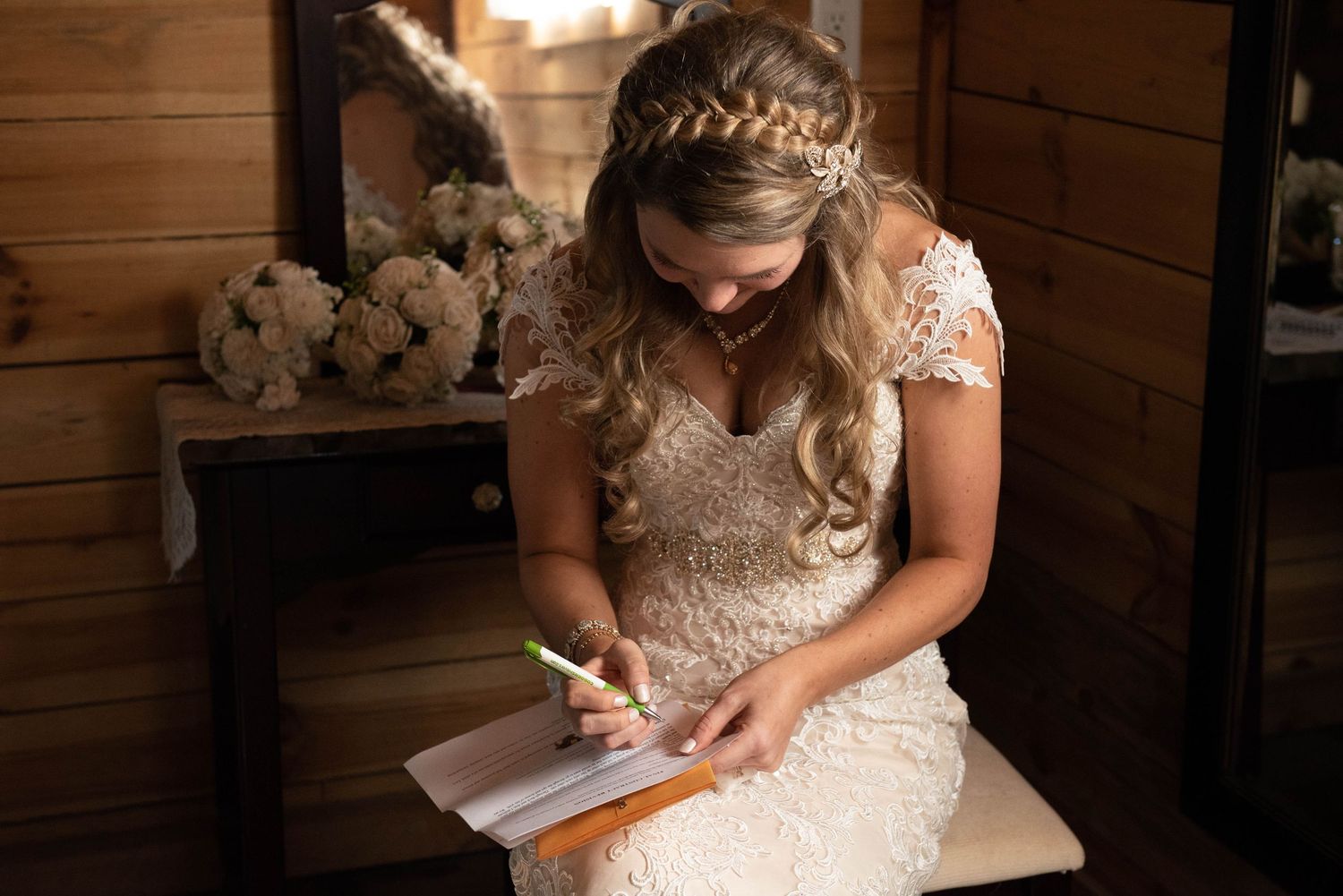 Bride in lace dress writes in journal while sitting in rustic wooden room. Rum River Barn Milaca Minnesota Weddings