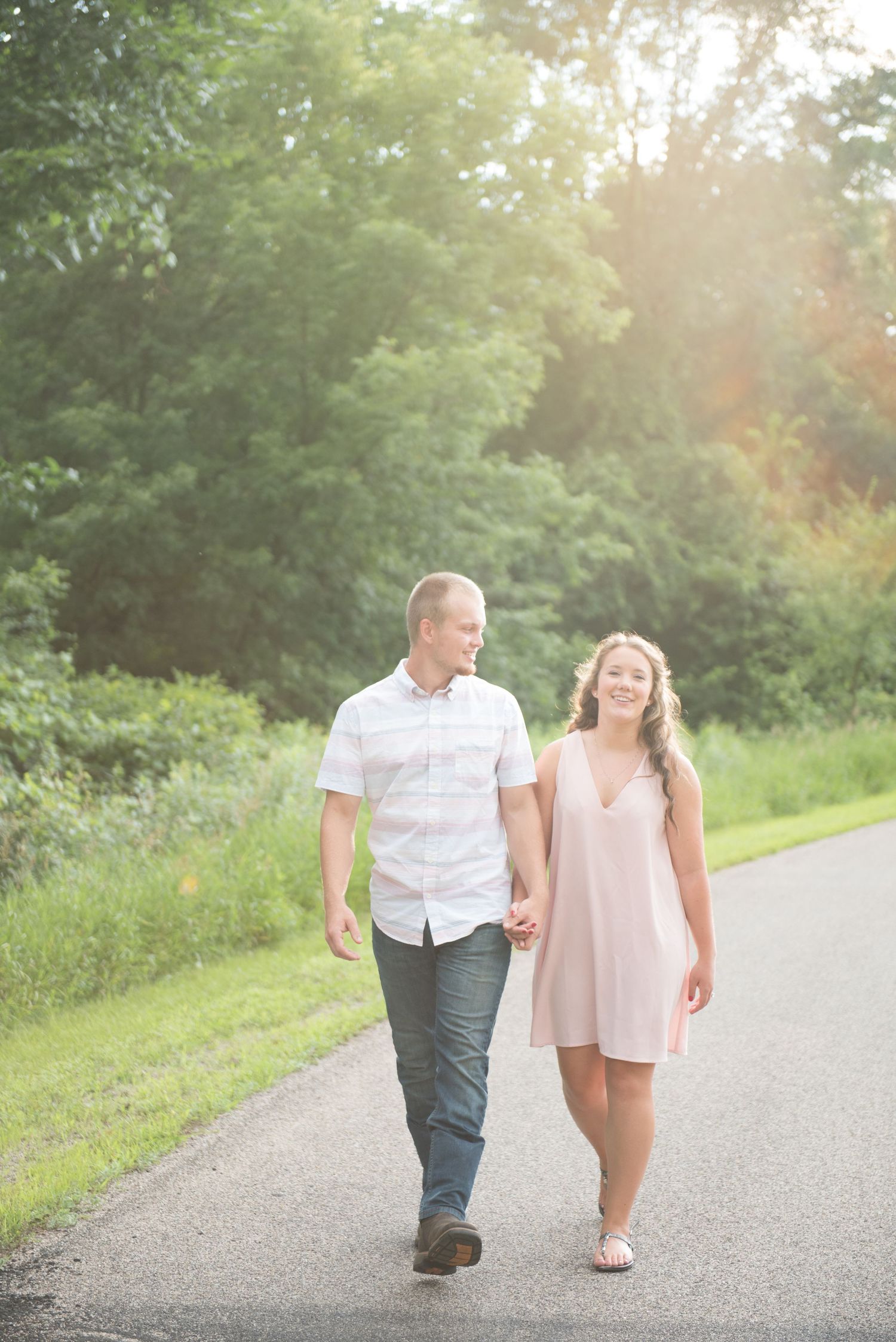 Two people stroll hand-in-hand down a peaceful country road at golden hour.