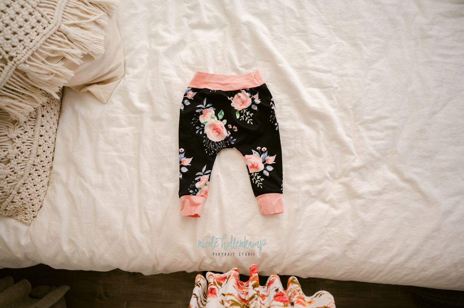 Black floral baby leggings with pink trim laid out on a white bedspread.
