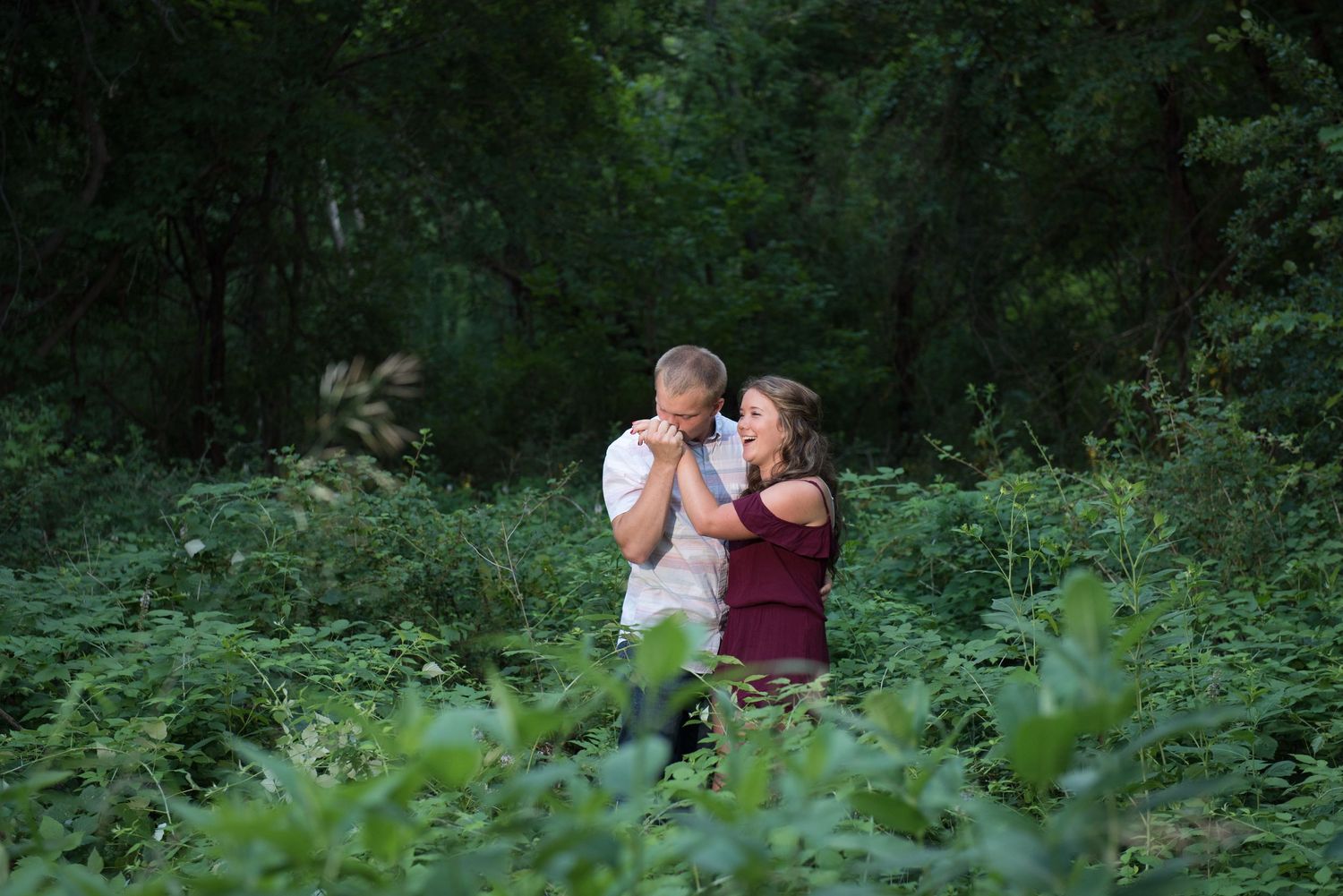 A couple shares an intimate moment among lush greenery in a wooded setting during a romantic photoshoot.