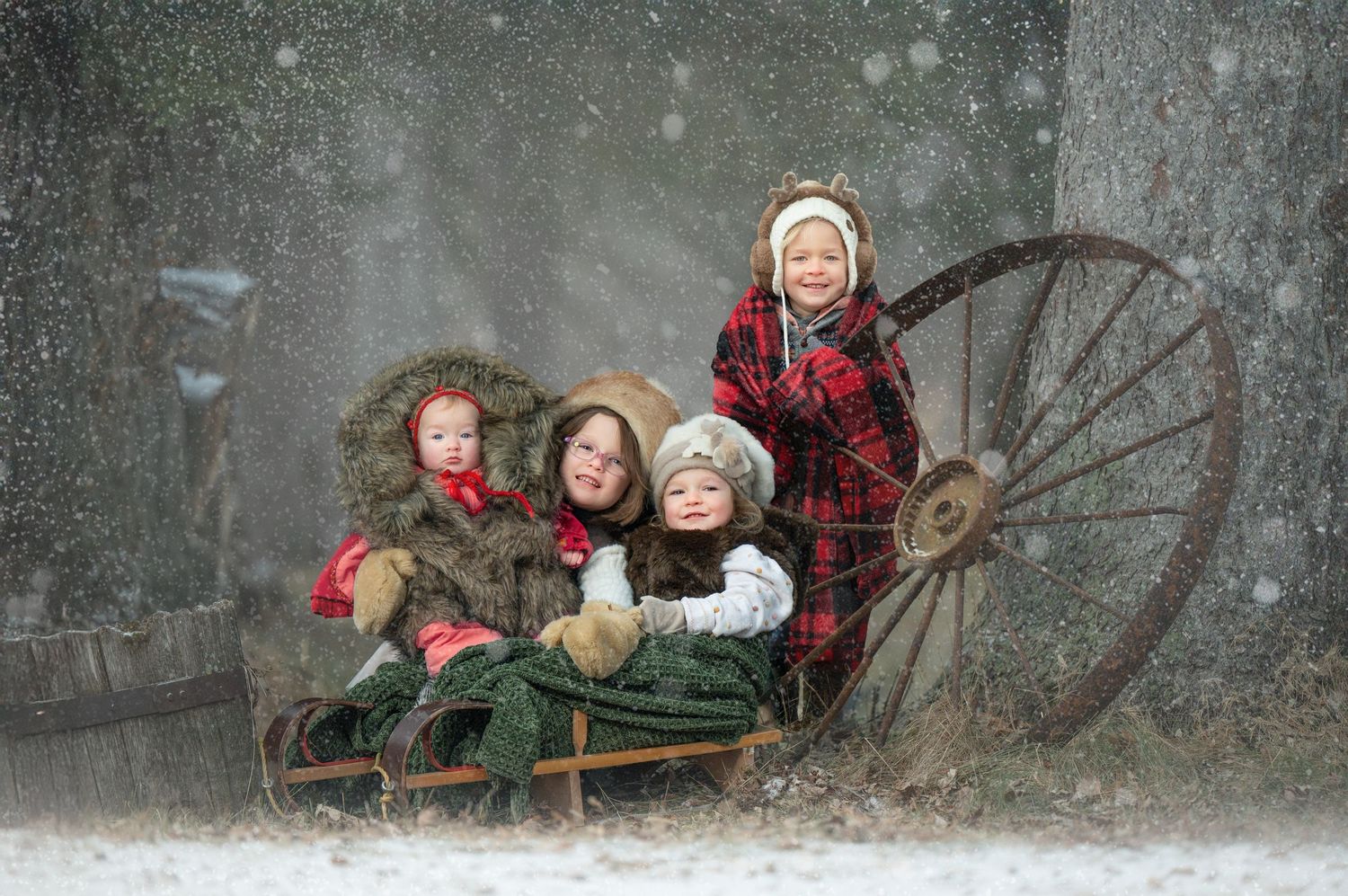 Joyful children on a vintage wooden sleigh in winter snow wearing red and green holiday attire.