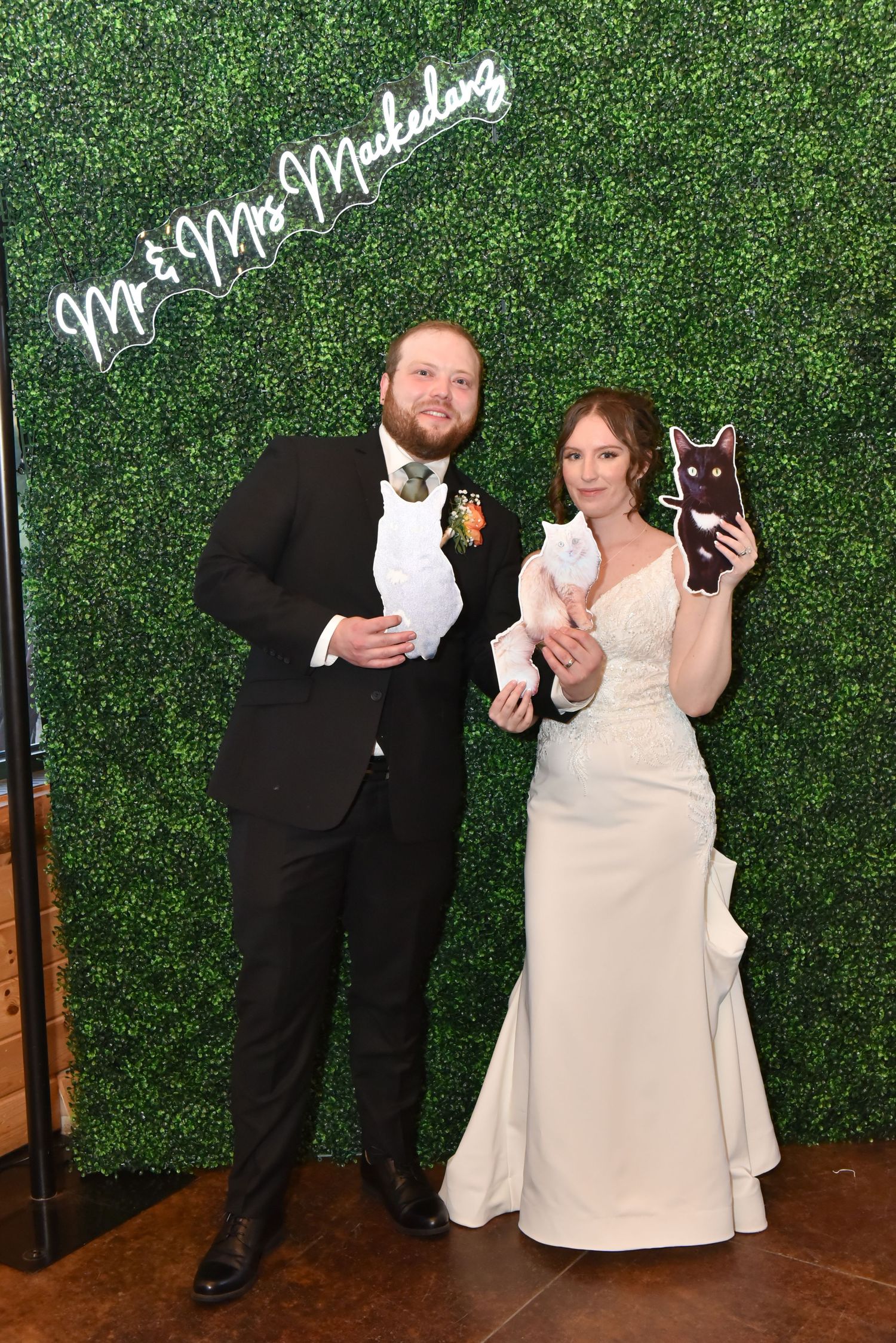 The Grands At Mulligans. Photo booth series of couple holding white cats against green hedge backdrop.