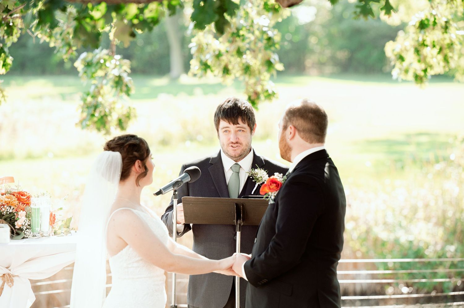 The Grands at Mulligans- Wedding Photos: ceremony takes place under trees with guests seated in rows outdoors.