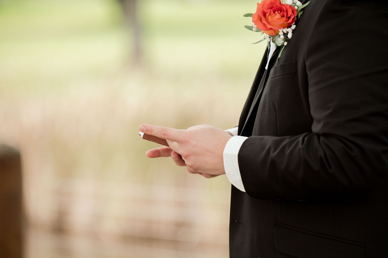 A pink rose boutonniere pinned to a dark suit jacket is shown in detail.