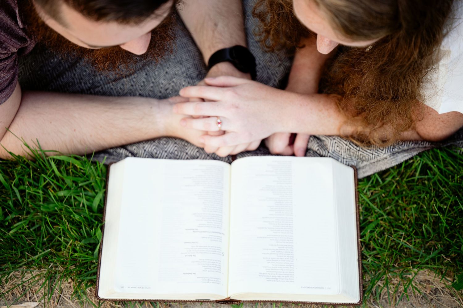 Books laid open on grass with couple relaxing together outdoors.