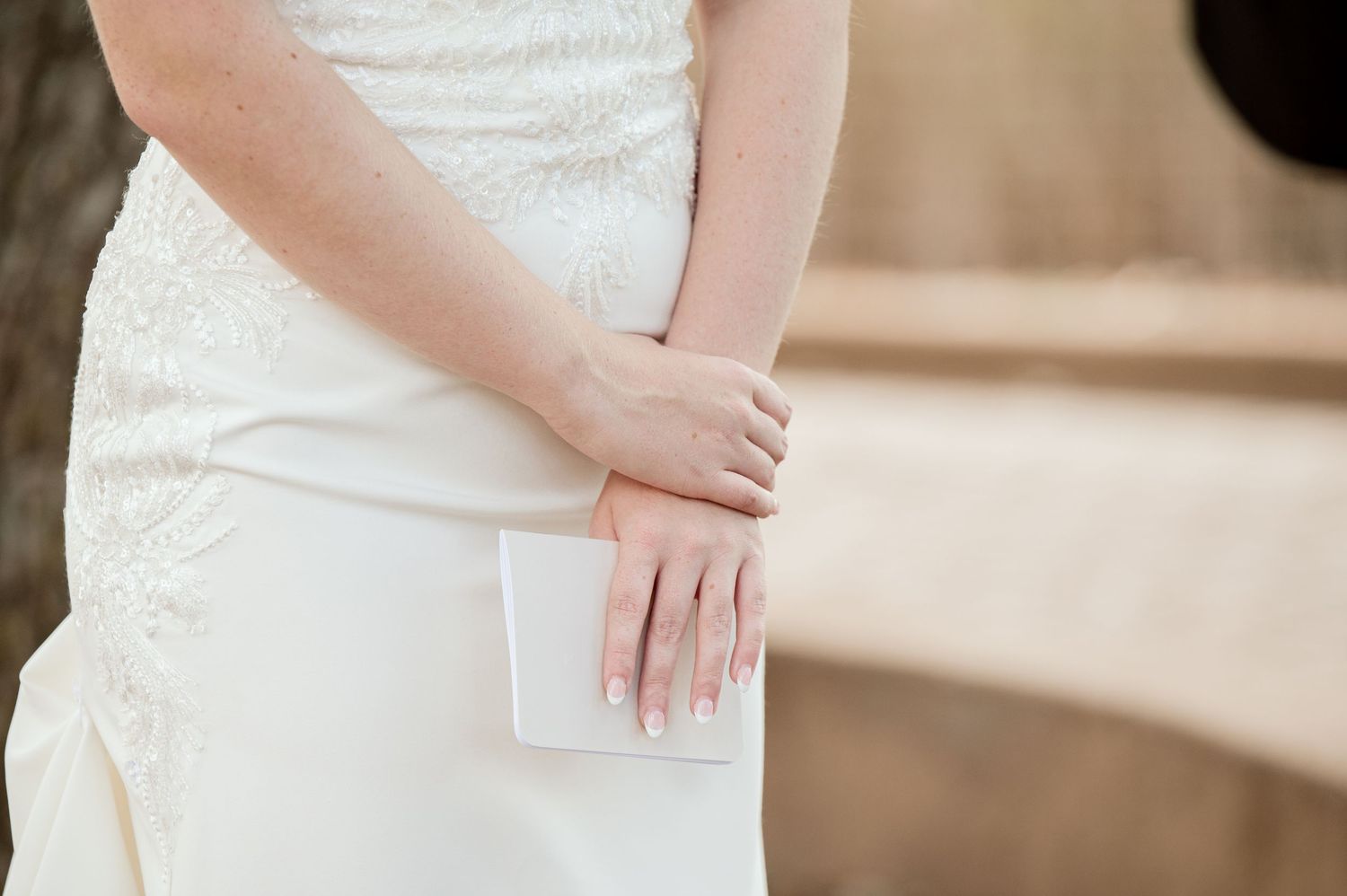 The Grands at Mulligans- Wedding Photos: Close-up of a bride in white dress holding papers during an outdoor wedding ceremony.