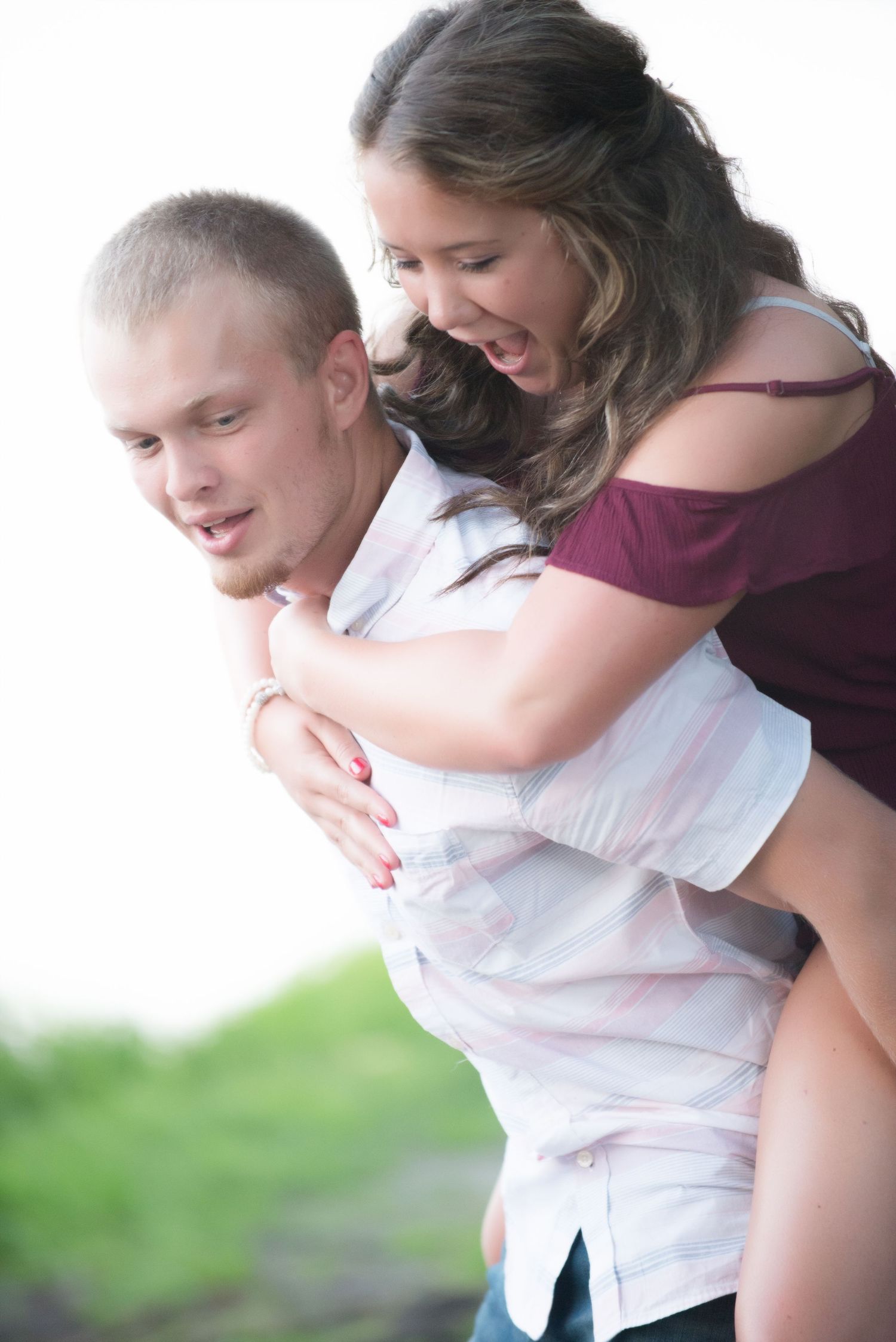 Playful couple embraces and laughs together during an outdoor photo session against a green background.