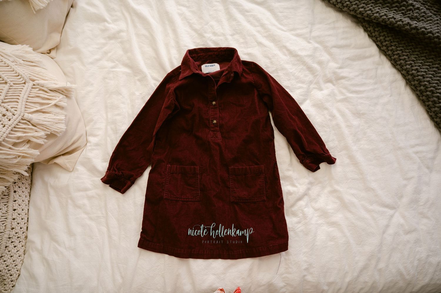 A burgundy corduroy coat with buttons lies flat on white bedding, displaying its classic vintage style.