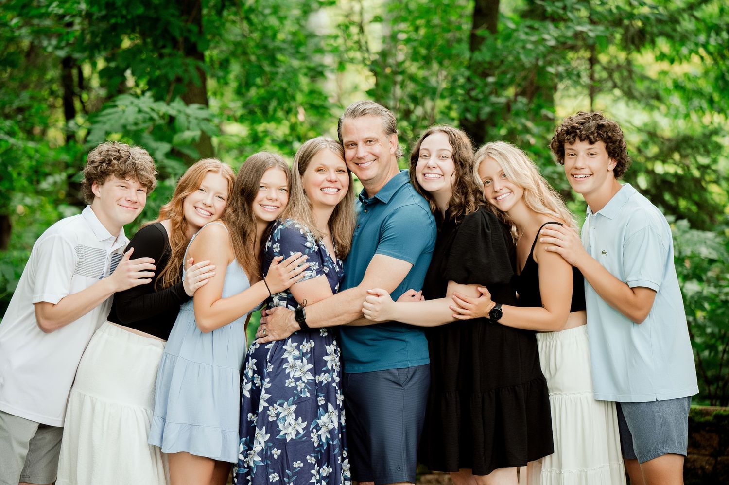 Clear Lake Family Photography: Group of friends laugh and smile together while posing outdoors in a lush green forest setting.