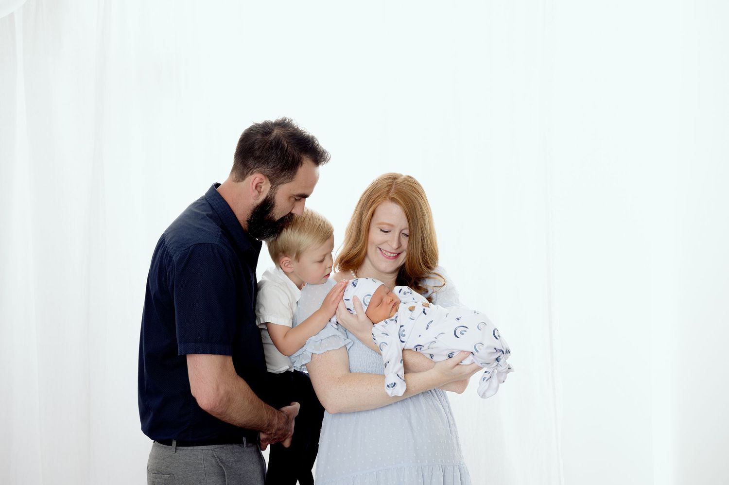 Sweet family portrait session with parents and two young children against a white backdrop.