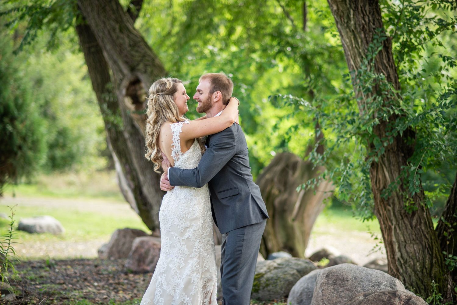A loving wedding embrace captured in a natural outdoor setting with trees and rocks in the background.