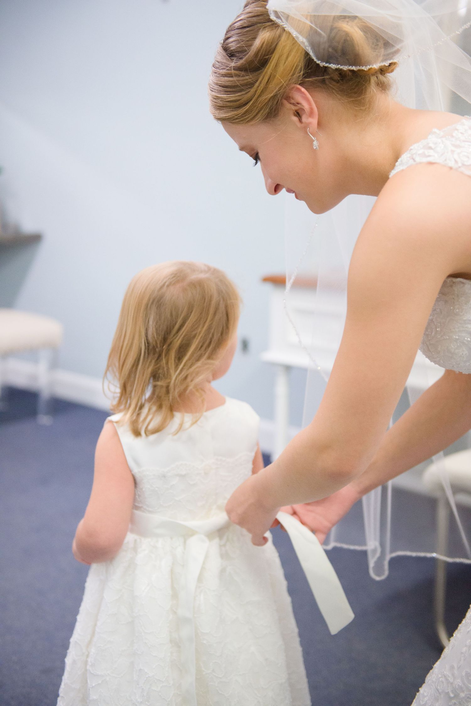 A tender moment in white as someone helps adjust a young girl's dress ribbon during a formal occasion. Andover wedding at Magestic Oaks Golf