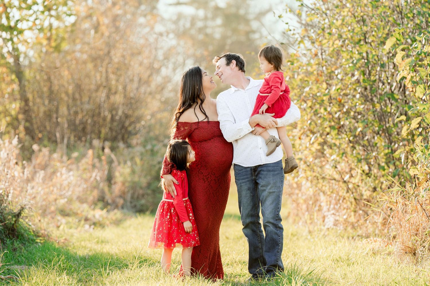 Family wearing coordinated red and white outfits pose together in autumn setting.