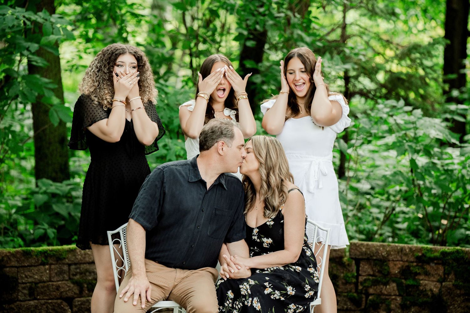 Clear Lake Family Photography: couple shares a kiss on a stone wall while three kids playfully cover their eyes
