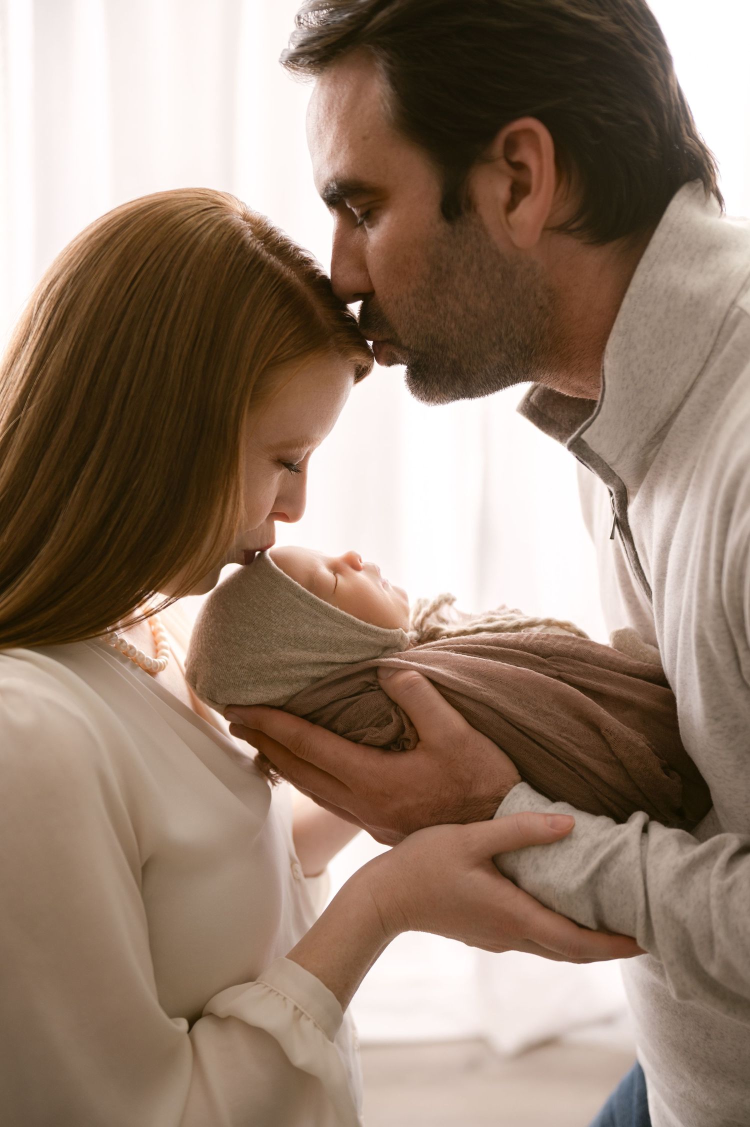 Tender family moment with newborn baby wrapped in soft beige blanket.