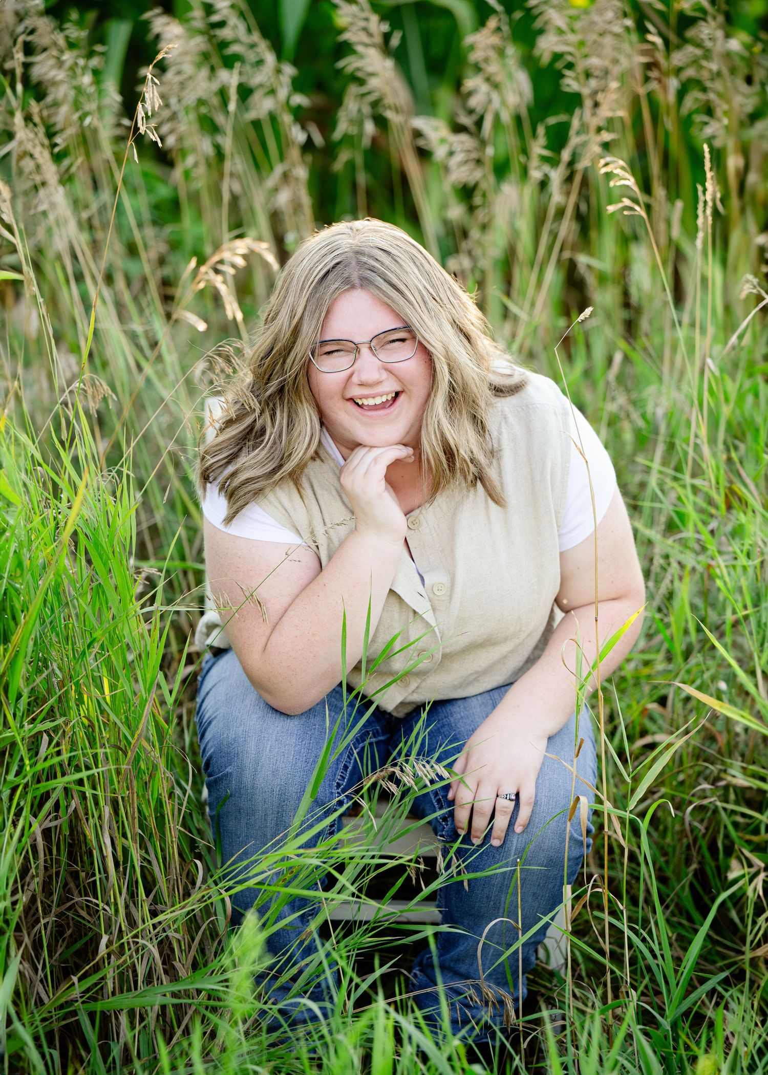 Senior Portrait in Foreston MN Person sitting in tall grass wearing jeans and white top during outdoor portrait session.