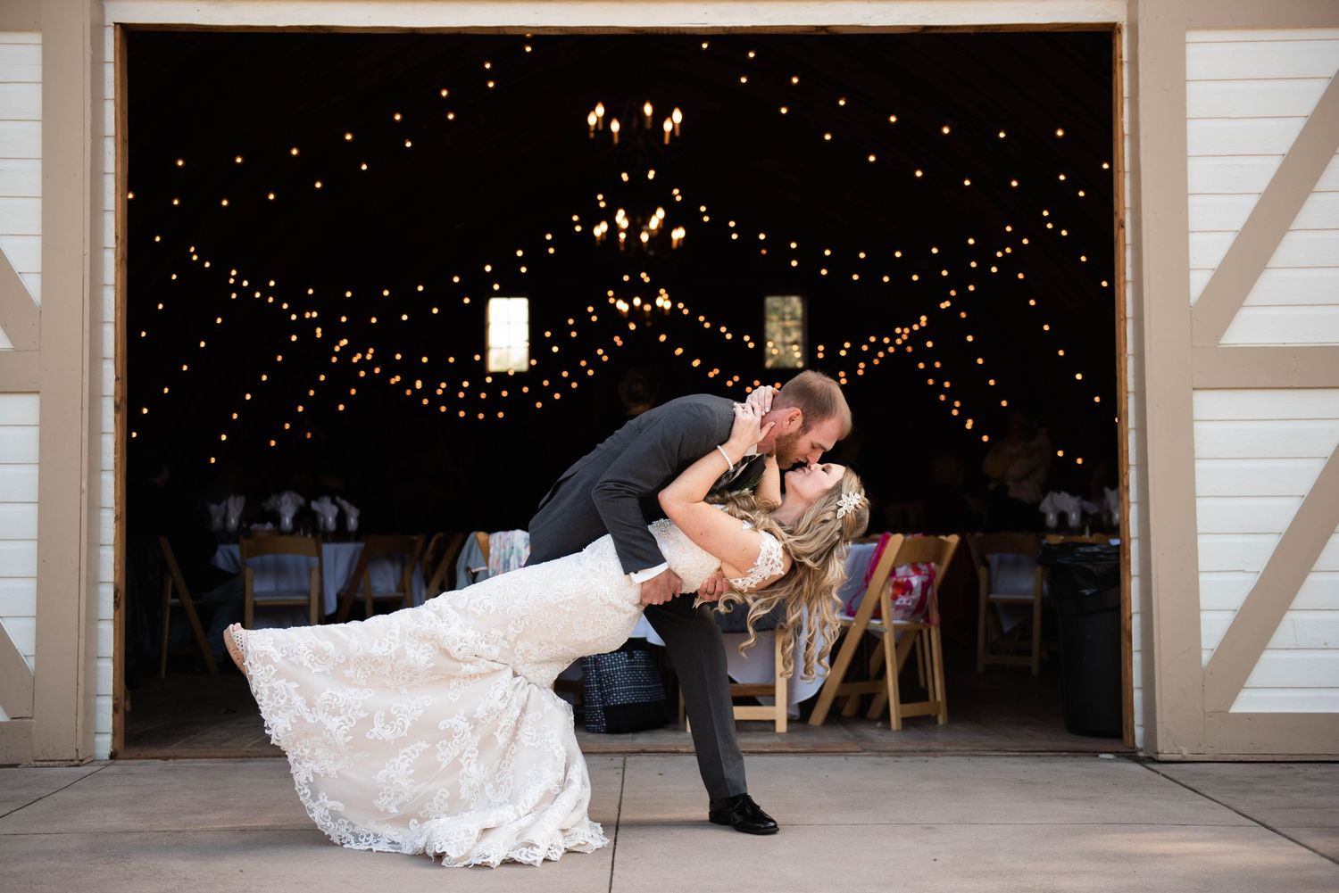 Romantic dance dip pose in barn venue with twinkling fairy lights creating magical atmosphere. Rum River Barn Milaca Minnesota Weddings