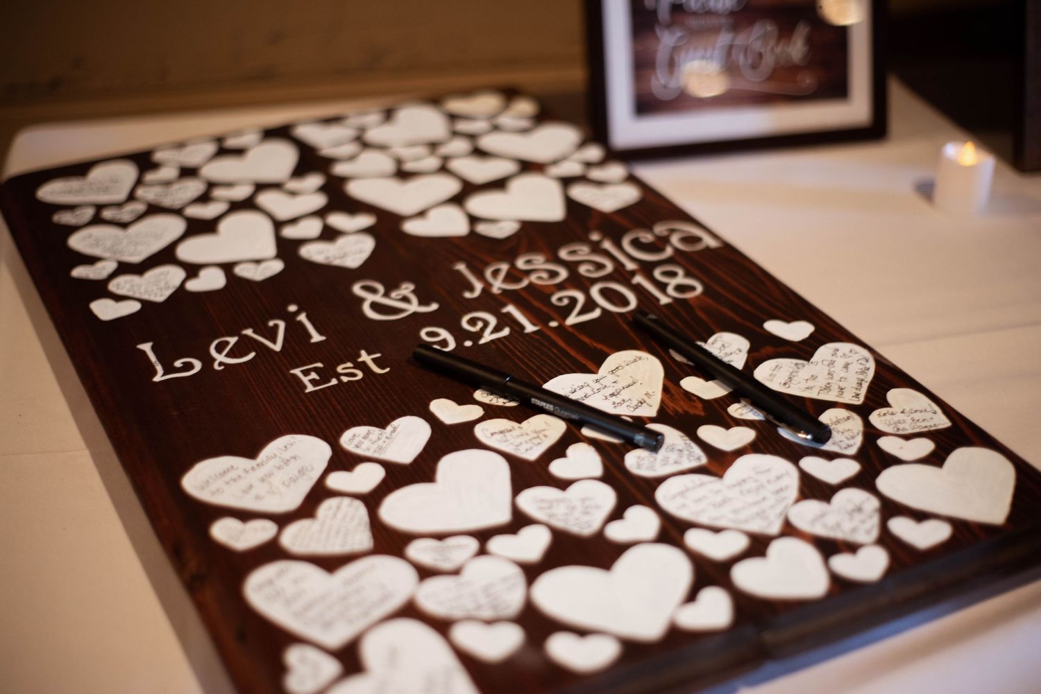 A wedding guest book alternative displays multiple small white paper hearts arranged neatly on a dark background.