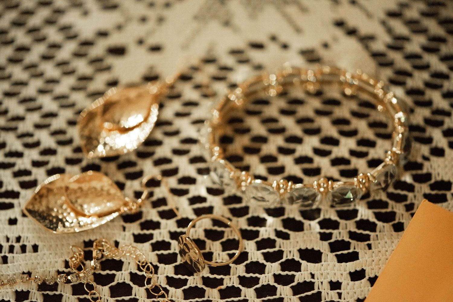 Elegant gold or bronze jewelry pieces displayed on a black mesh or lace textured surface.