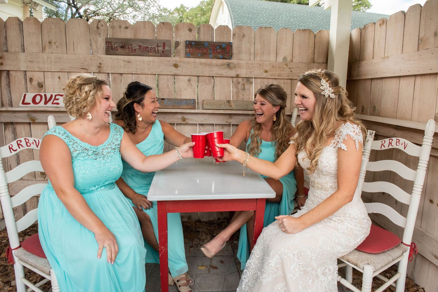 A group celebrates with red cups at a wooden table while wearing turquoise dresses. Rum River Barn Milaca Minnesota Weddings
