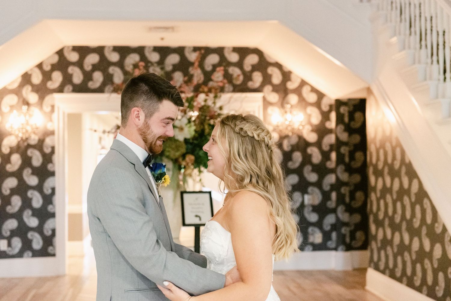 A romantic moment between newlyweds under an arched doorway with patterned wallpaper.