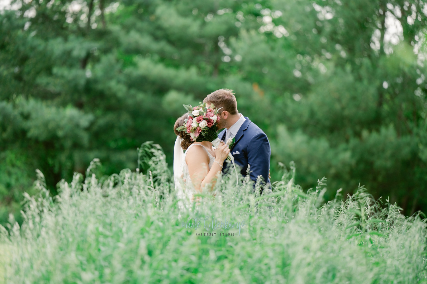 A couple shares an intimate moment in a field of tall wispy grass with evergreen trees in the background. Taken in a Golf Course in MN