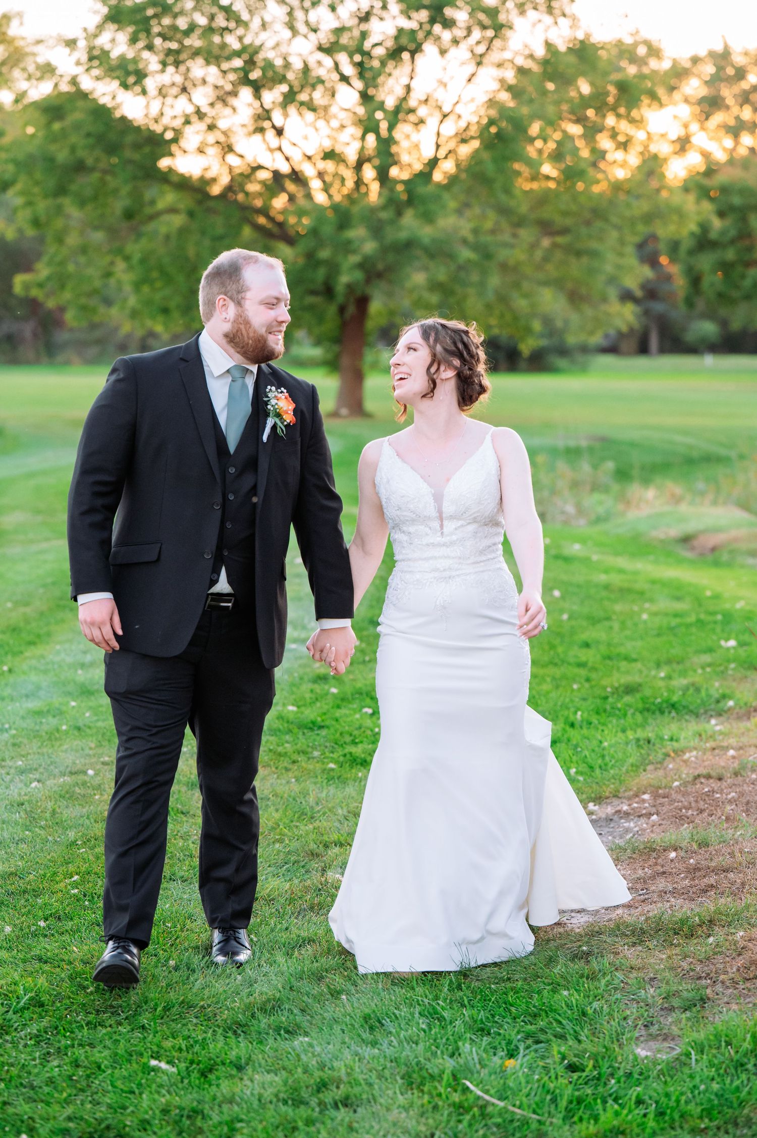 affordable st cloud area wedding photographer MN.A couple shares a loving glance while walking on grass during golden hour at their wedding.