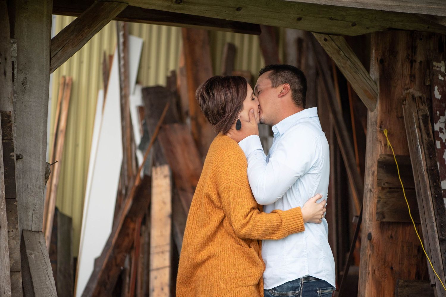 A couple sharing an intimate moment under a wooden beam structure with flowing curtains in the background.