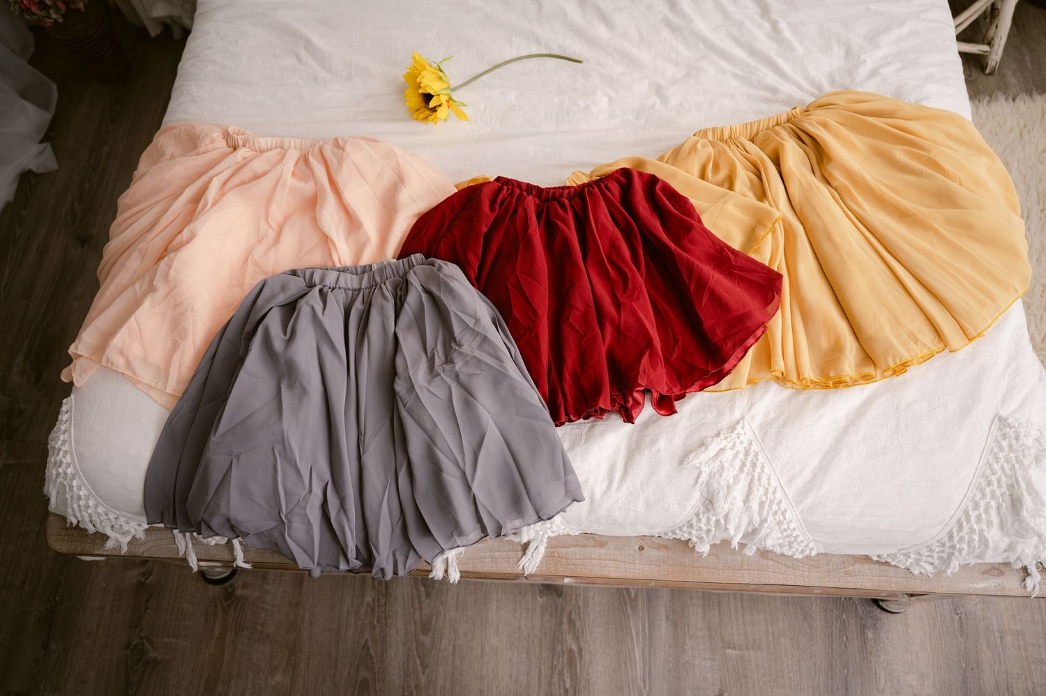 Four tulle skirts in gray, red, beige and peach colors laid out on a white bedspread.